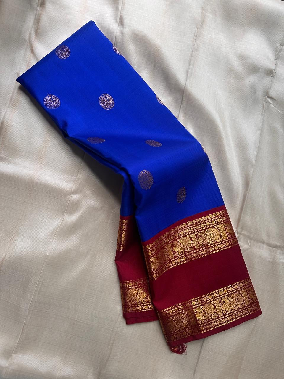 Pure Kanchipuram silk saree in royal blue with scattered round silver motifs and a maroon zari woven border along the edge.