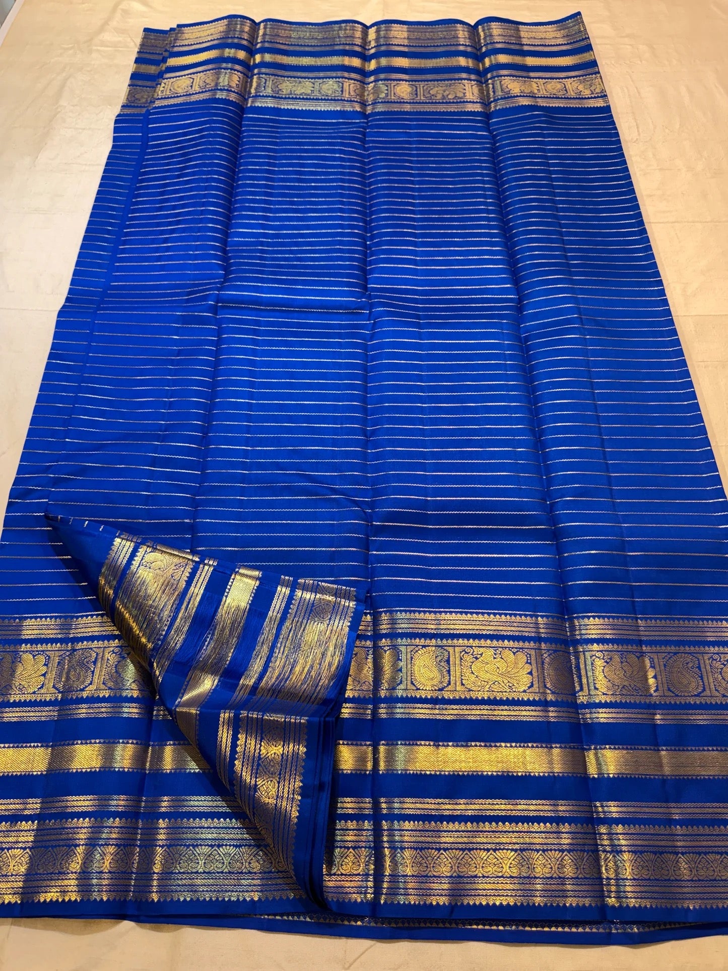 Close-up of the antique-gold peacock zari border on a royal blue Kanjivaram Vairaoosi saree