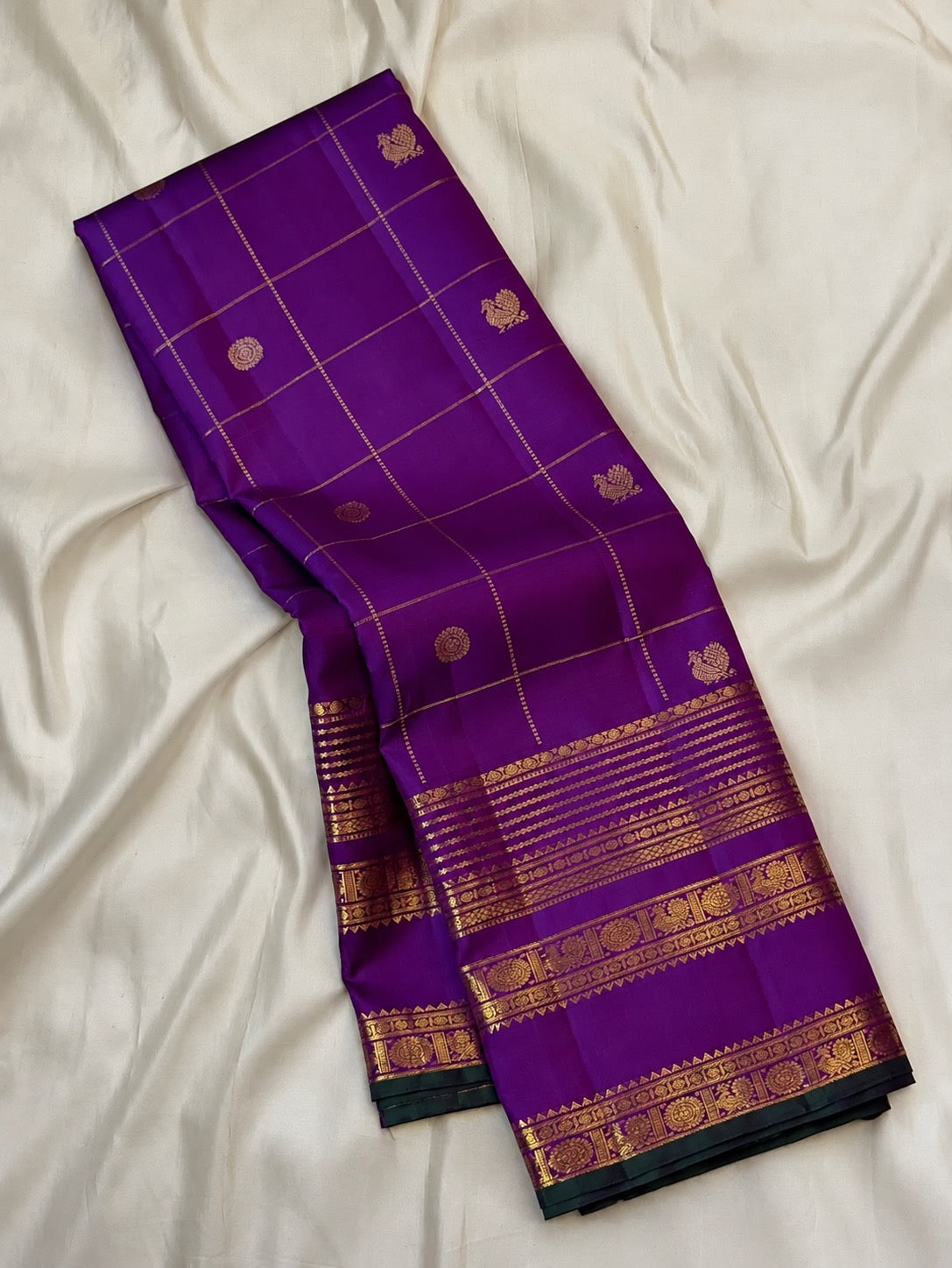 Royal purple Pure Silk Kanjivaram Zari Kattam saree folded with antique-gold Varisaipet border and green edge.