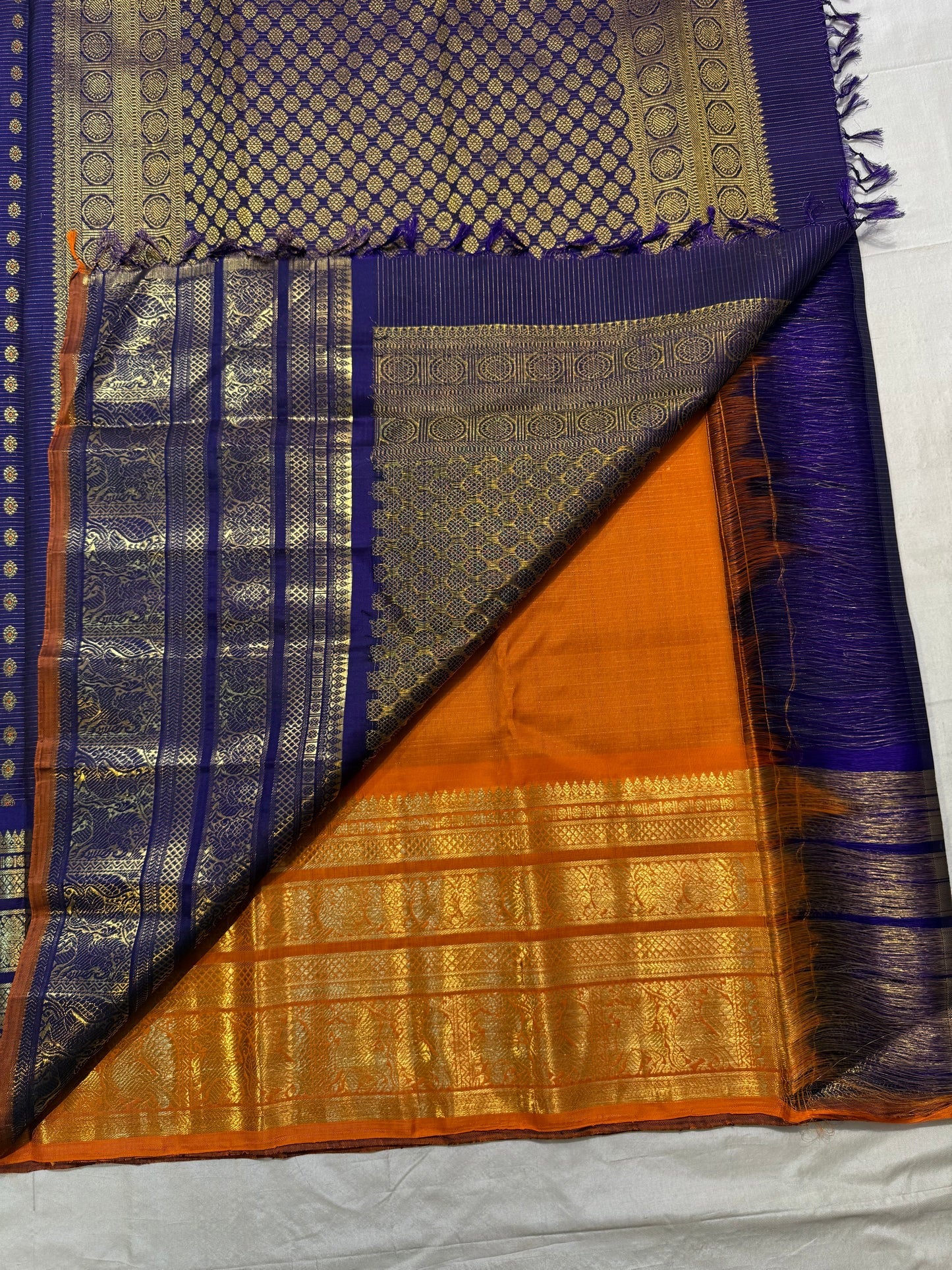 Folded violet Vairaoosi saree highlighting broad layered gold zari border and Burnt Orange finishing edge