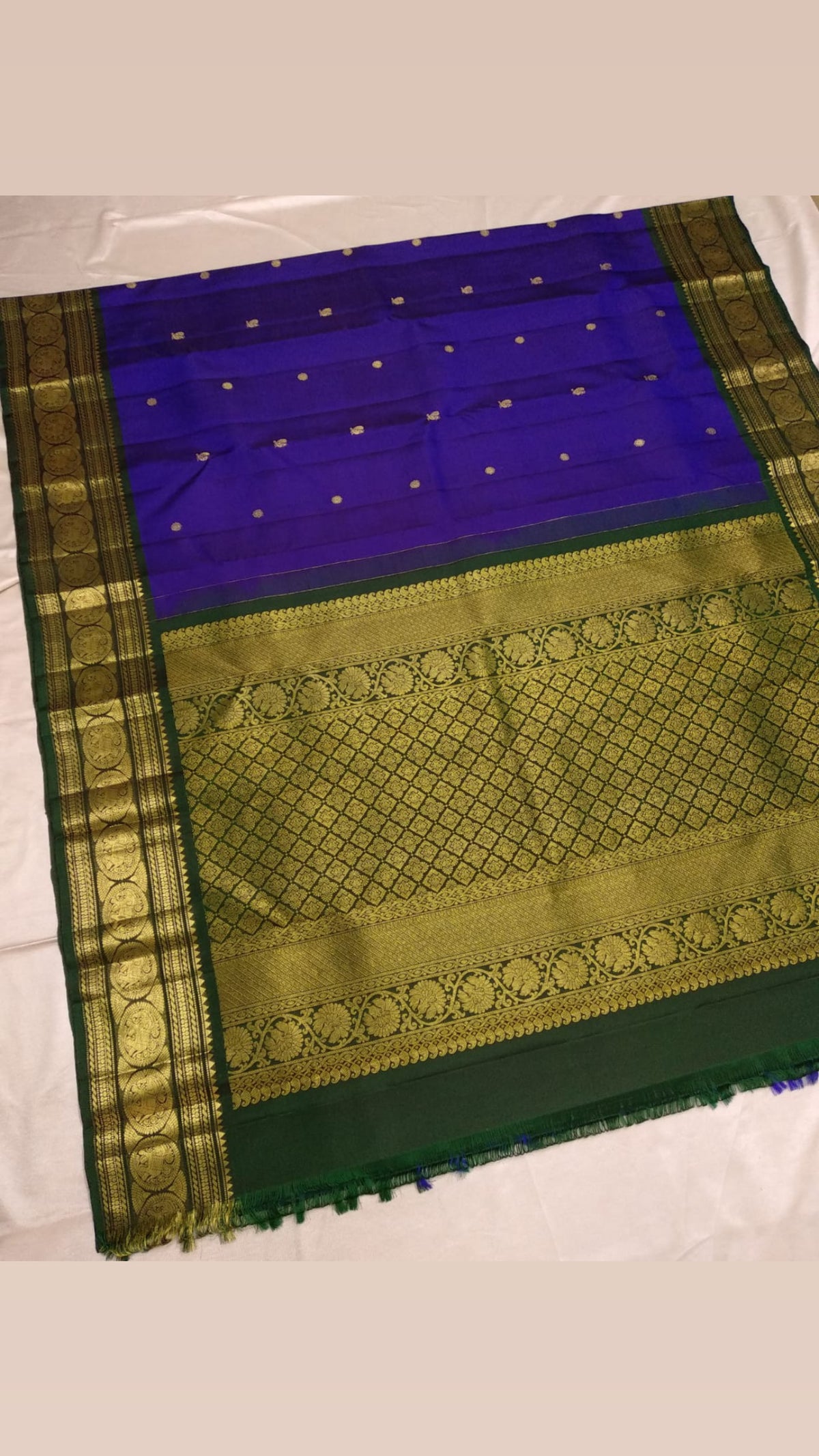 Royal-violet pure silk Kanchipuram saree folded to show petite gold buttas and bottle-green Sorgavaasal Mayil border with circular ornamental frames.