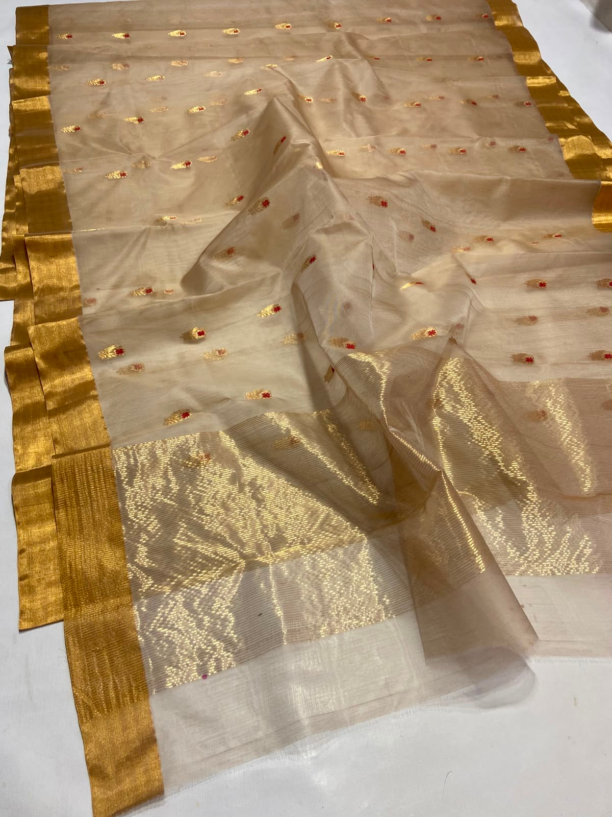 Folded Sandalwood Beige Katan Silk Chanderi saree showing gold border and petite gold buttas with red accents.