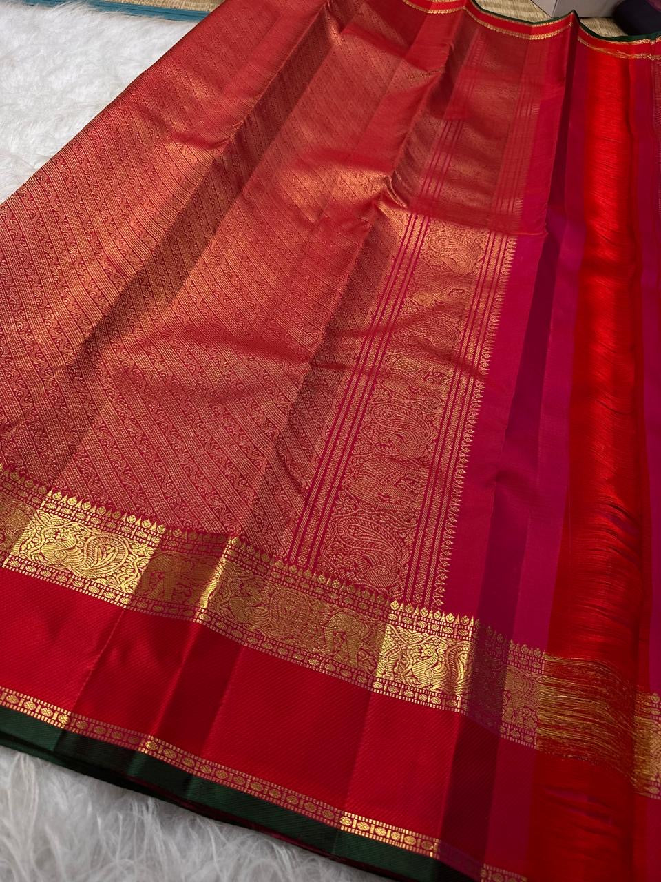 Handwoven raspberry and vermilion Kanchipuram Zari Kattam saree displayed with its elaborate gold zari border and pallu.