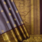 Folded slate-lavender Kanchipuram silk saree with small zari buttas and a broad Kaapi Brown peacock border