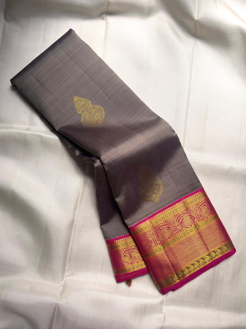 Smoky Charcoal Grey Pure Silk Kanchipuram Korvai saree with gold zari buttas and vibrant Rani Pink peacock border.
