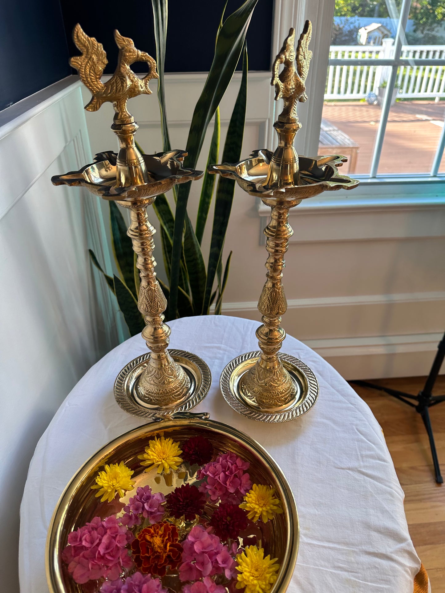 Pair of traditional brass Kuthu Vilakku lamps in a home setting with decorative flower bowl
