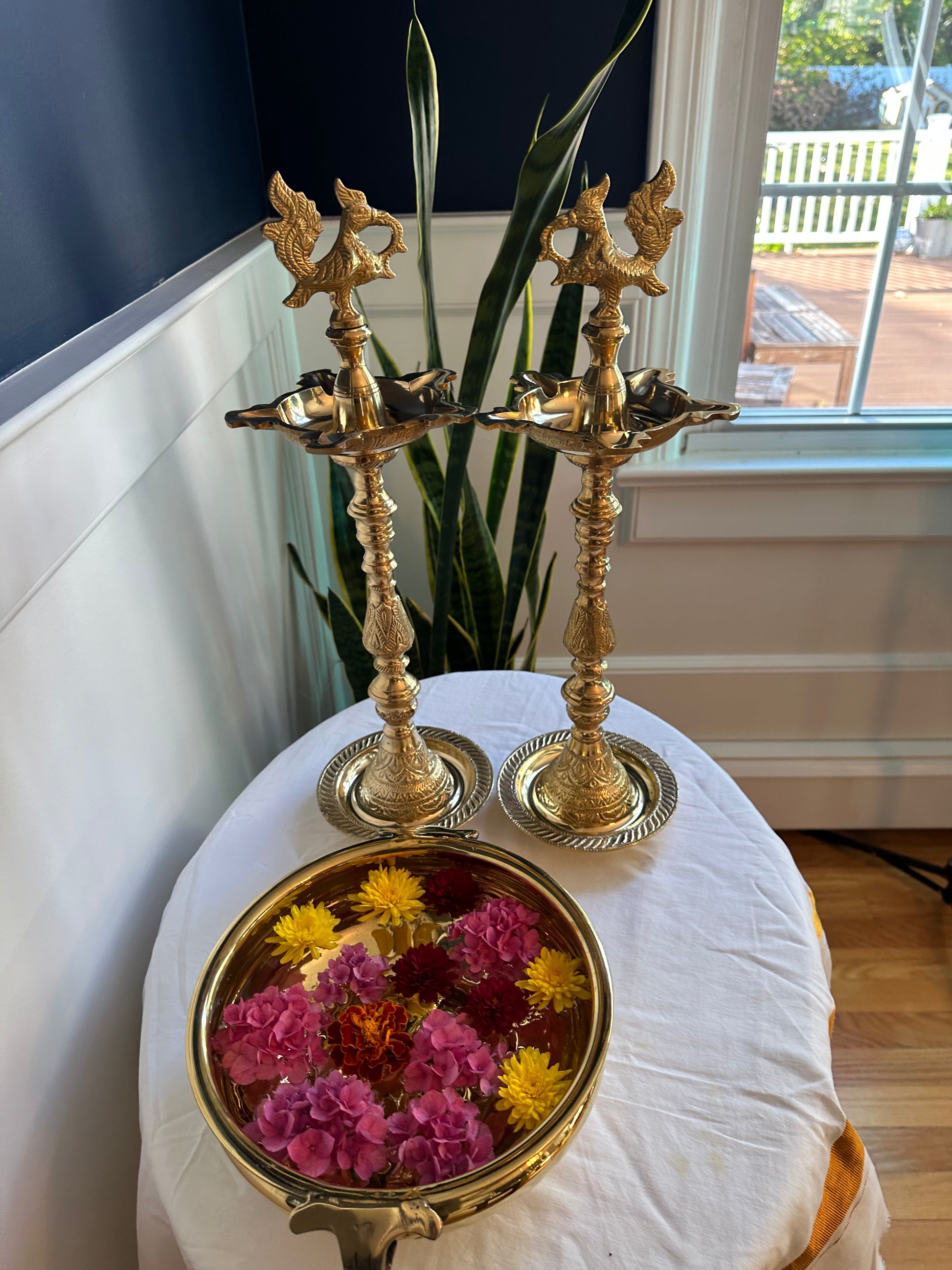 Solid brass Kuthu Vilakku oil lamps placed near window with floral brass urli bowl