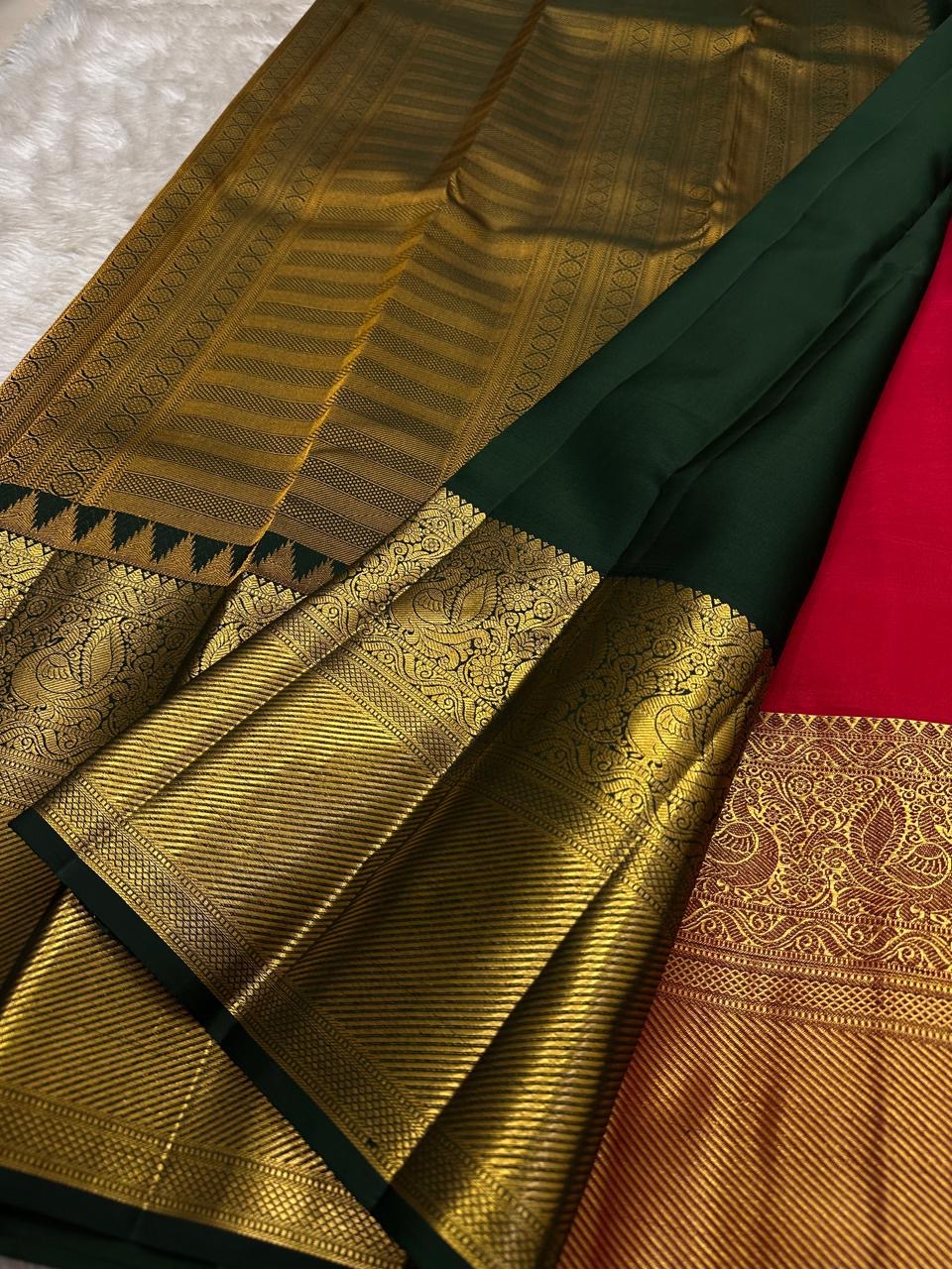 Close-up of gold zari woven border with deep green edging beside the red saree body on a light fabric background.