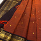 Angled close-up of rust Pure Kanchipuram silk saree with small gold zari buttas, black border, and orange tassels beside the pallu.