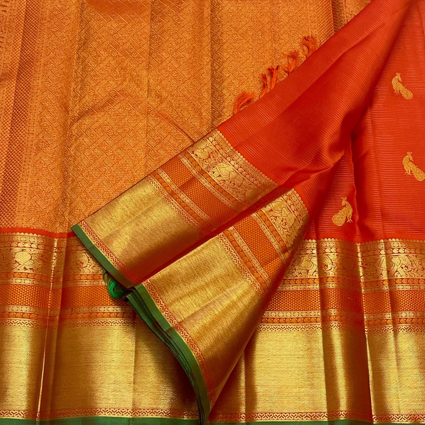 flat lay vermillion orange kanchipuram silk saree showing paisley buttas and zari border