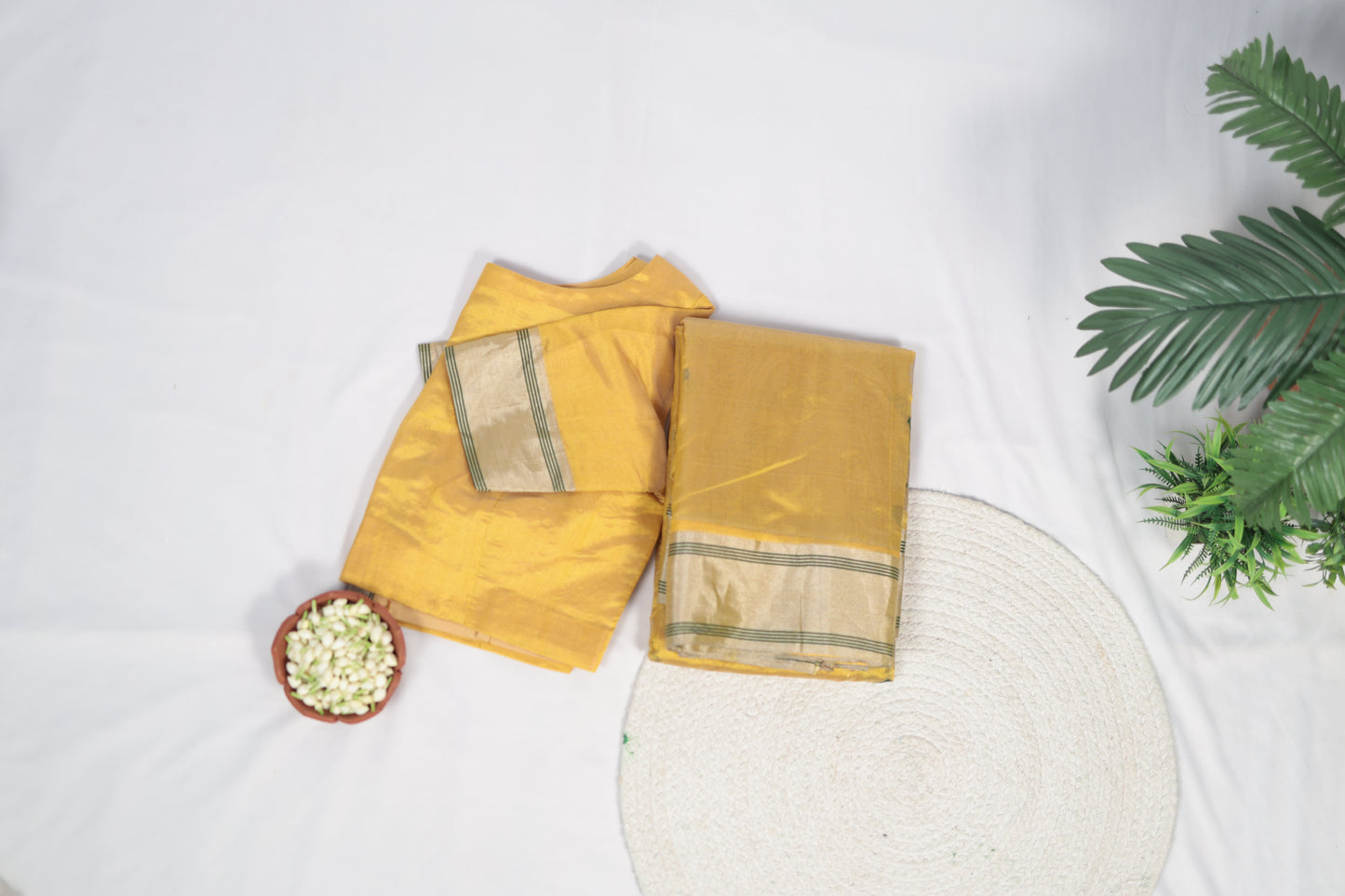 Overhead flat-lay of folded sunflower yellow Chanderi silk saree placed beside a round mat and small bowl, showing border and body color.