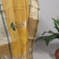 Folded sunflower yellow Chanderi silk saree displayed lengthwise, showing repeating white floral buttas and a gold zari border with green lines.