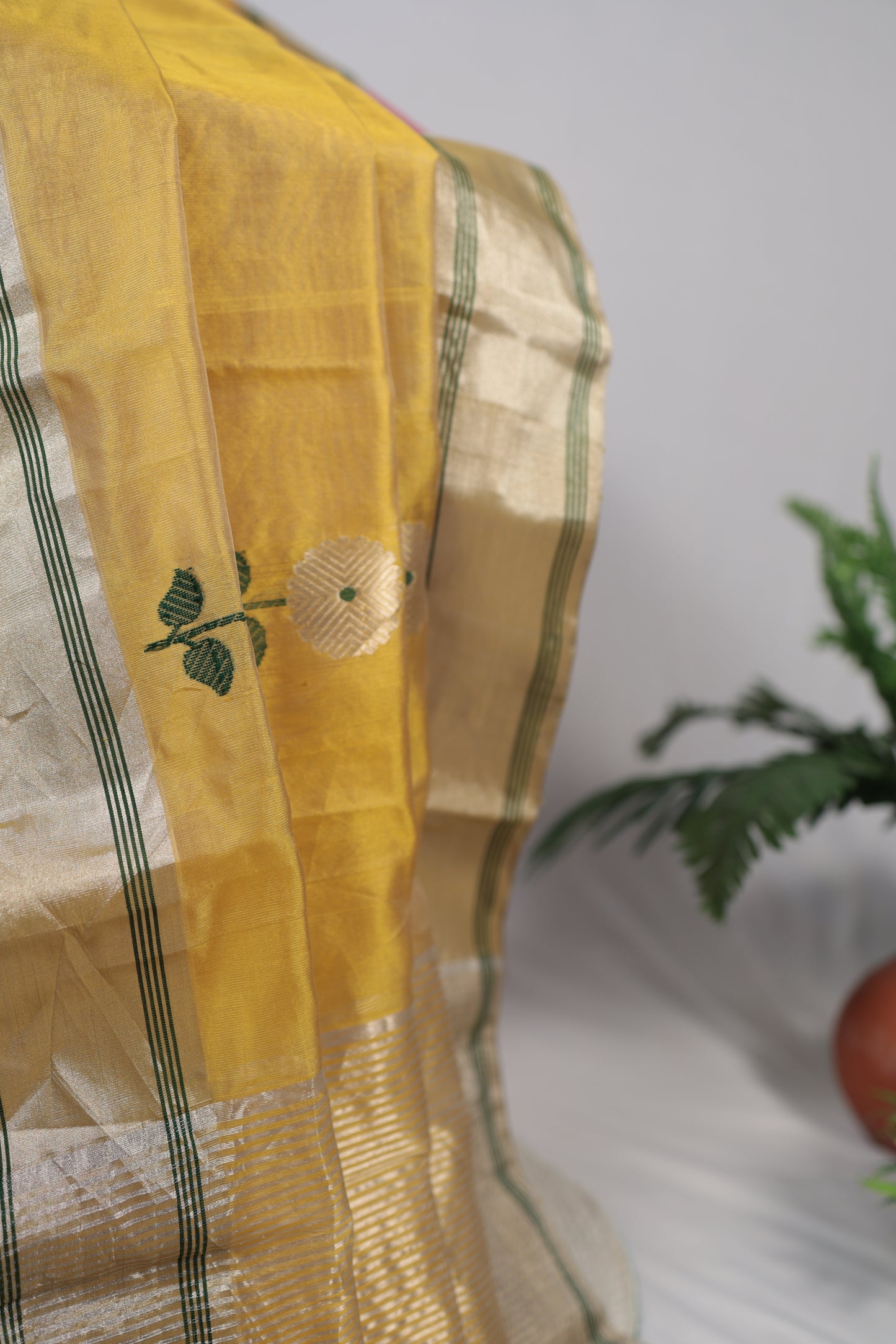 Folded sunflower yellow Chanderi silk saree displayed lengthwise, showing repeating white floral buttas and a gold zari border with green lines.