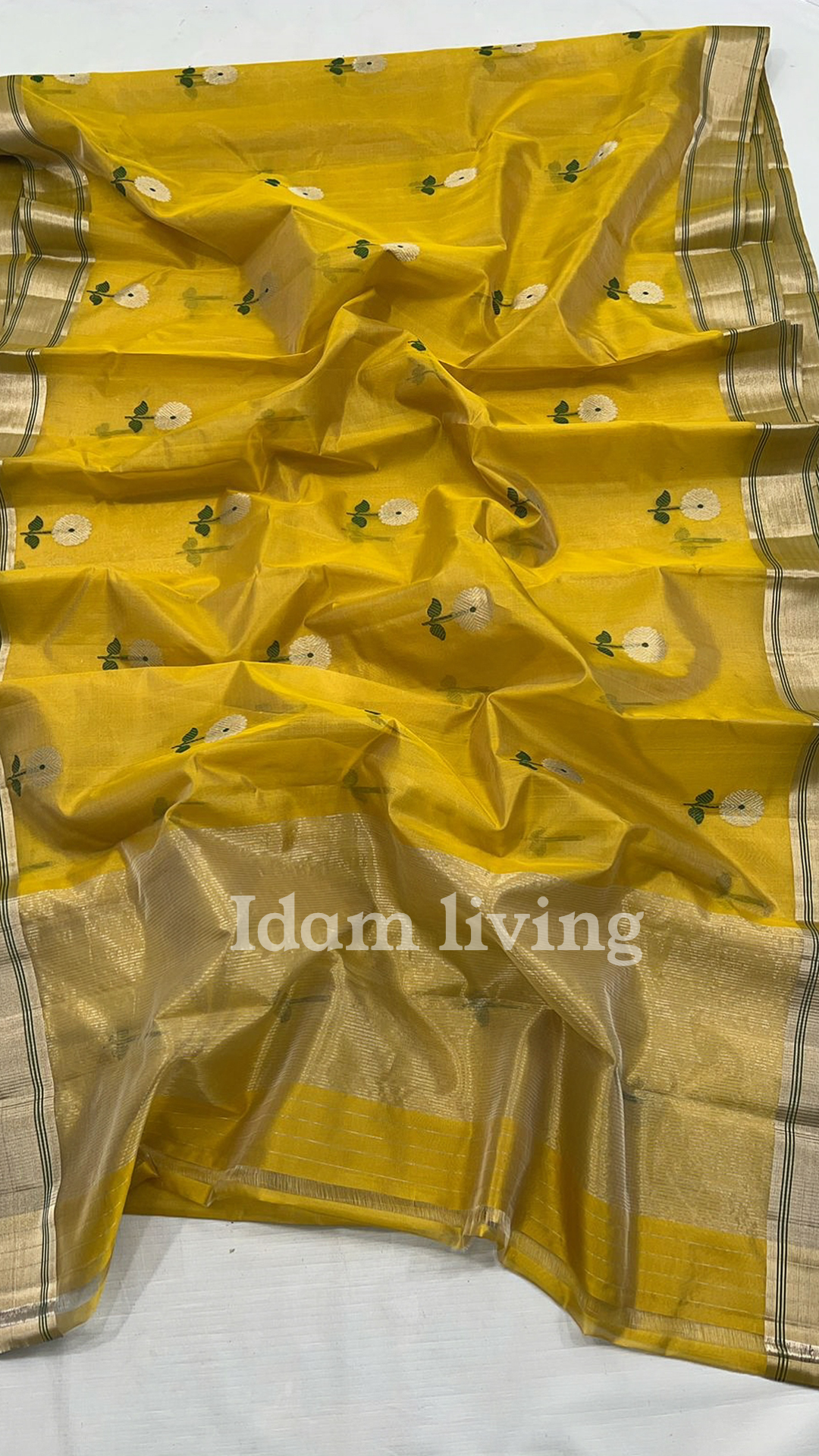 Full body view of a model wearing a sunflower yellow Chanderi silk saree with white floral buttas and gold zari border against a brown backdrop.