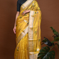 Flat-lay of folded sunflower yellow Chanderi silk saree on a white surface, showing gold zari border with fine green stripe detailing.