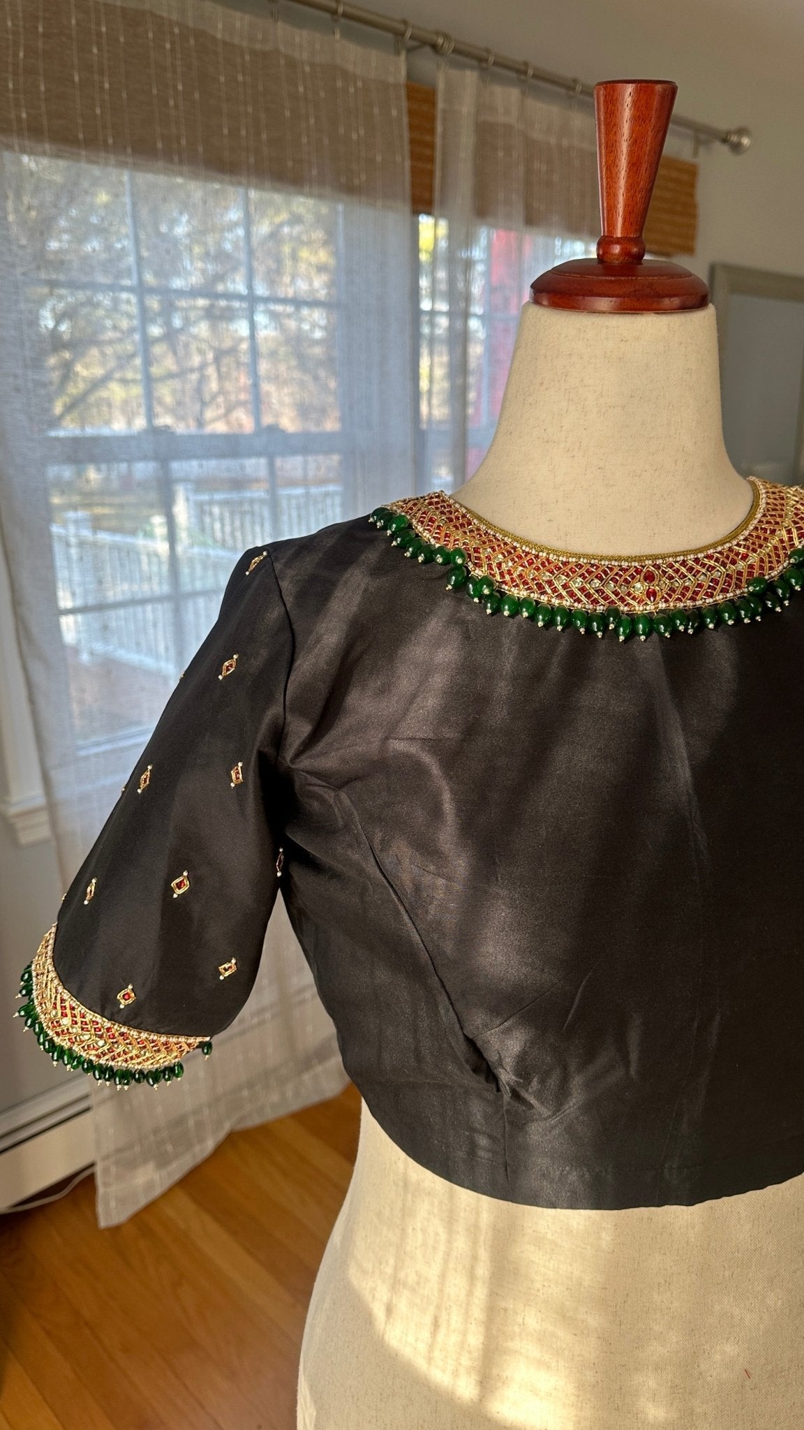 Flat lay of black silk cotton Tanjore designer blouse with intricate kemp embroidery