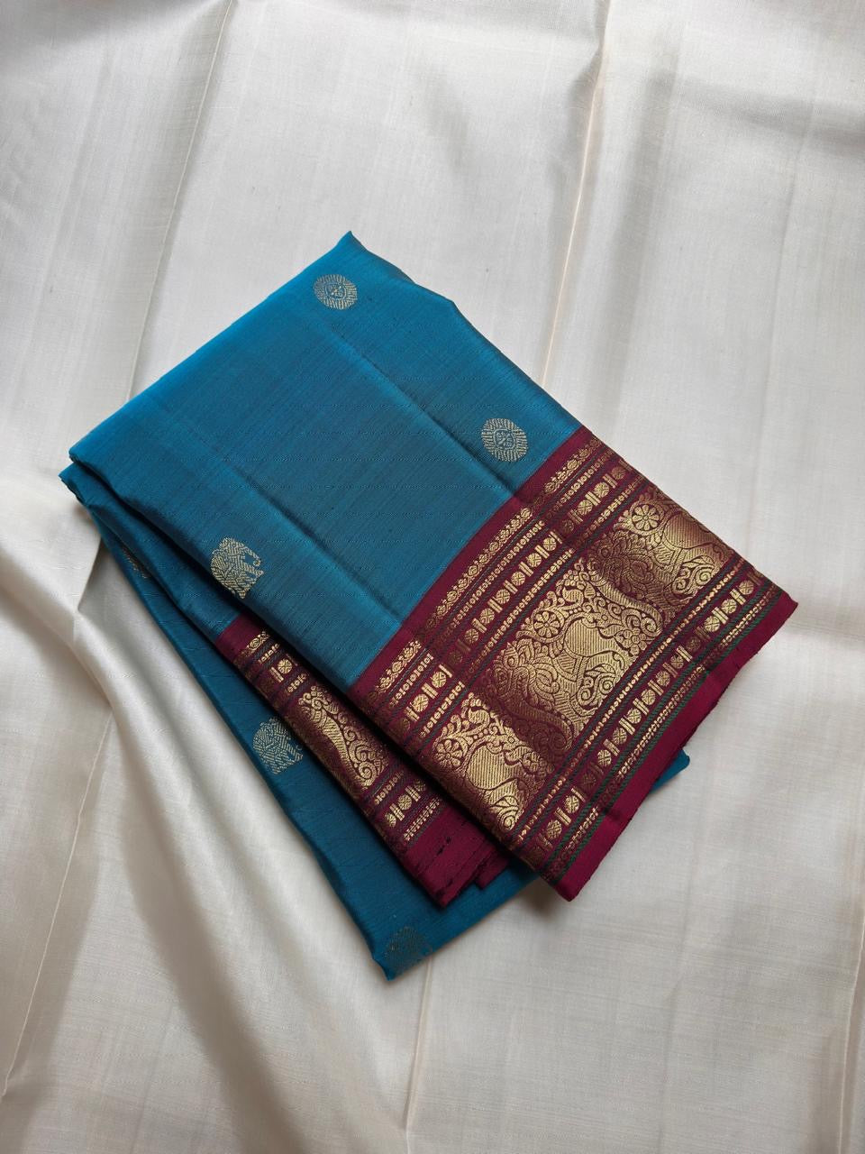 Saturated blue-green Kanchipuram silk body scattered with traditional classic-gold zari buttas.