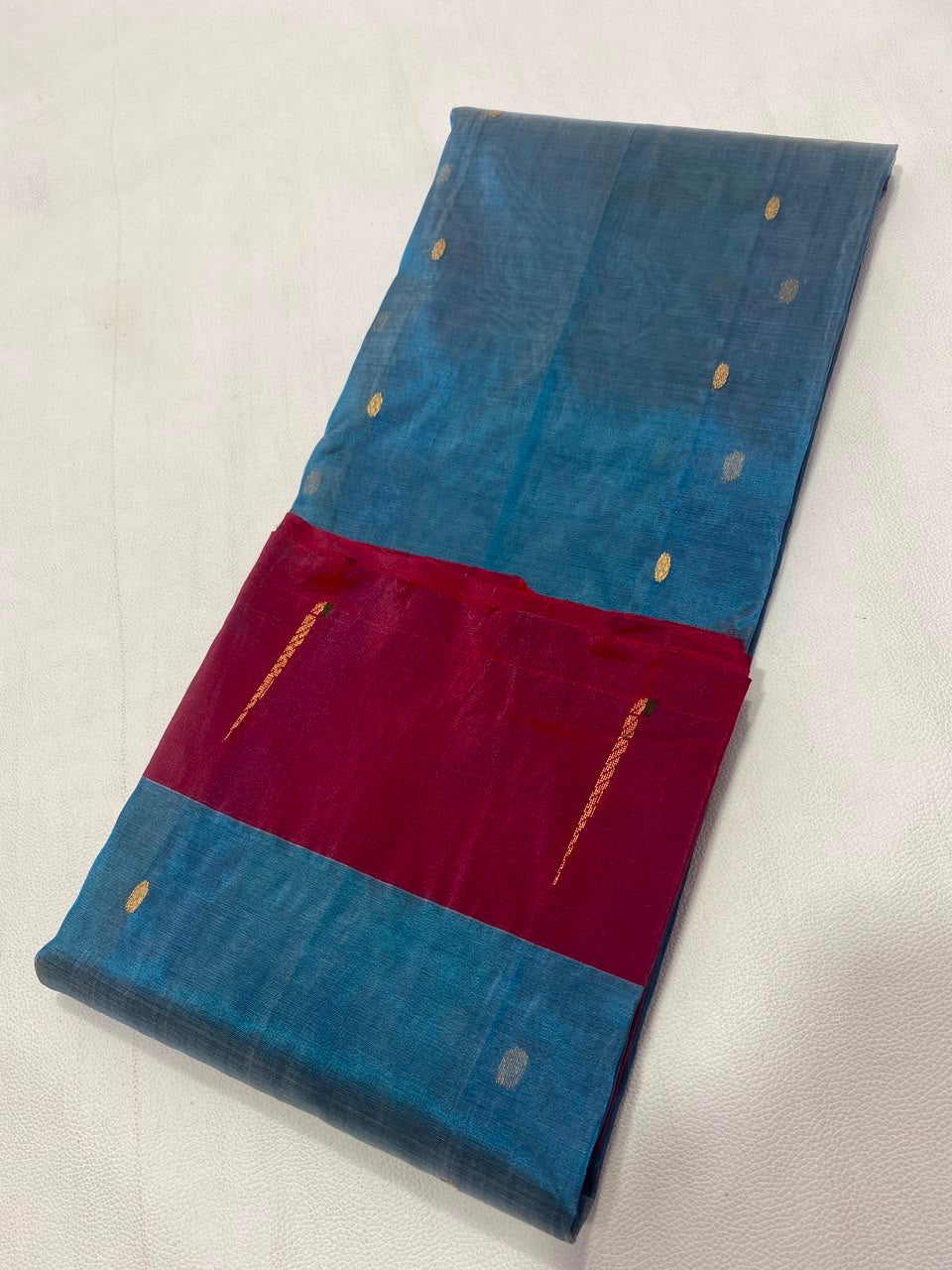 Folded Teal Blue Tissue Silk Chanderi saree with sparse gold and silver-toned woven buttas.