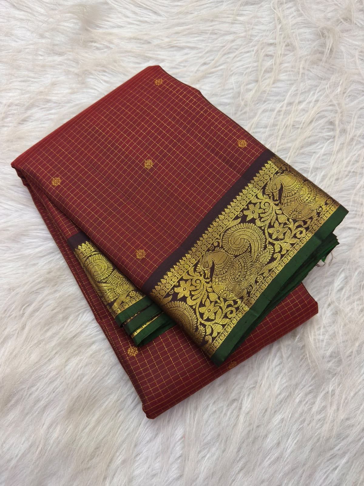 Vermilion red Kanchipuram silk saree folded, showing checked body, plum peacock border and pallu