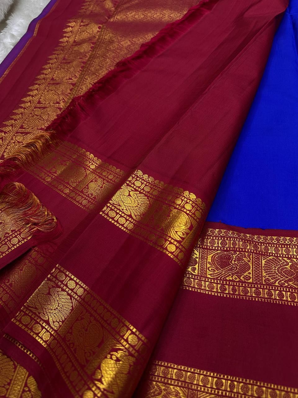 Close view of maroon pallu with dense gold zari woven detailing beside the royal blue saree body and border.
