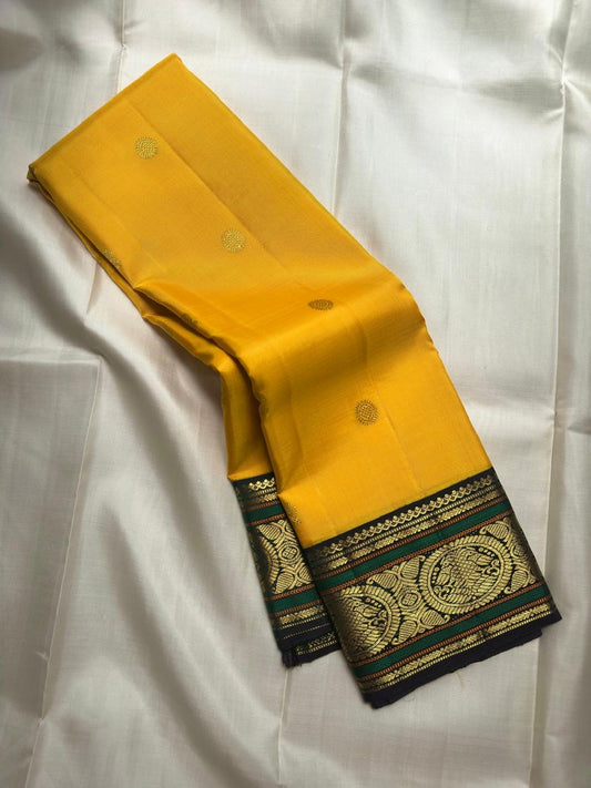 Folded yellow Kanchipuram saree showing deep green gold zari Mayil border.
