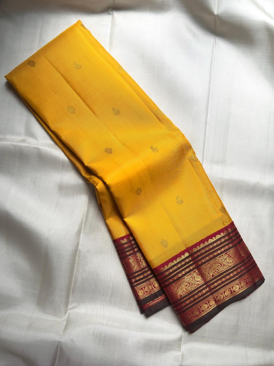 Open Turmeric Yellow Korvai saree showing scattered gold buttas and intricately layered deep Maroon zari border.