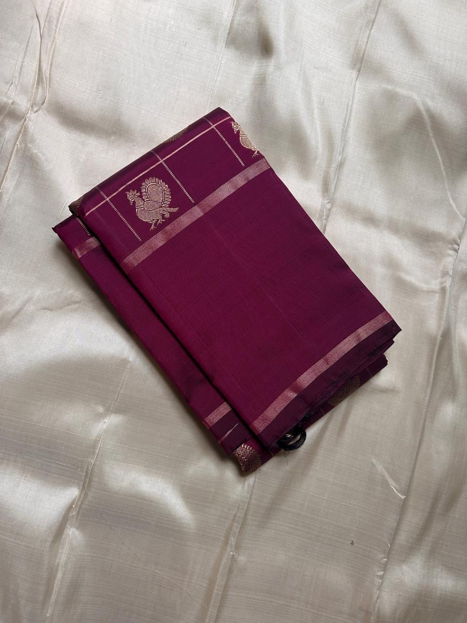 Folded plum Pure Kanchipuram silk saree showing zari checked grid and small woven motif on an ivory backdrop.