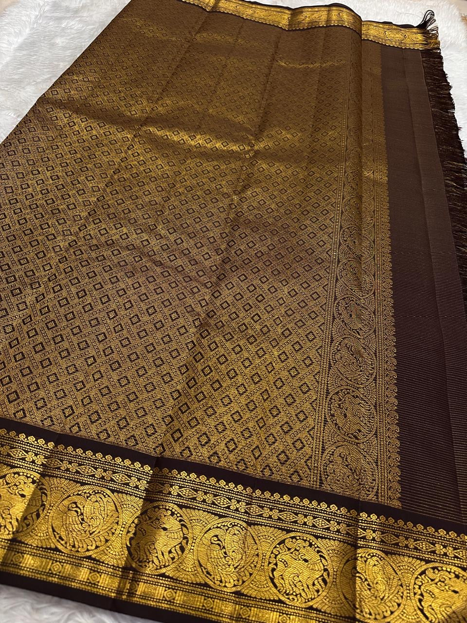 Deep brown Kancheepuram silk saree folded showing Vairaoosi body with Kamalam butta and ornate self-colour Mayil gold zari border