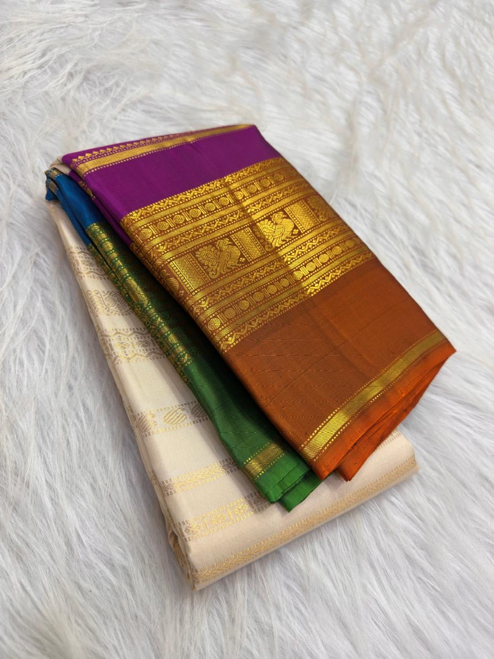Folded VarnaJaalam Pure Silk Kanchipuram saree showing purple, green, blue and burnt-orange zari borders.