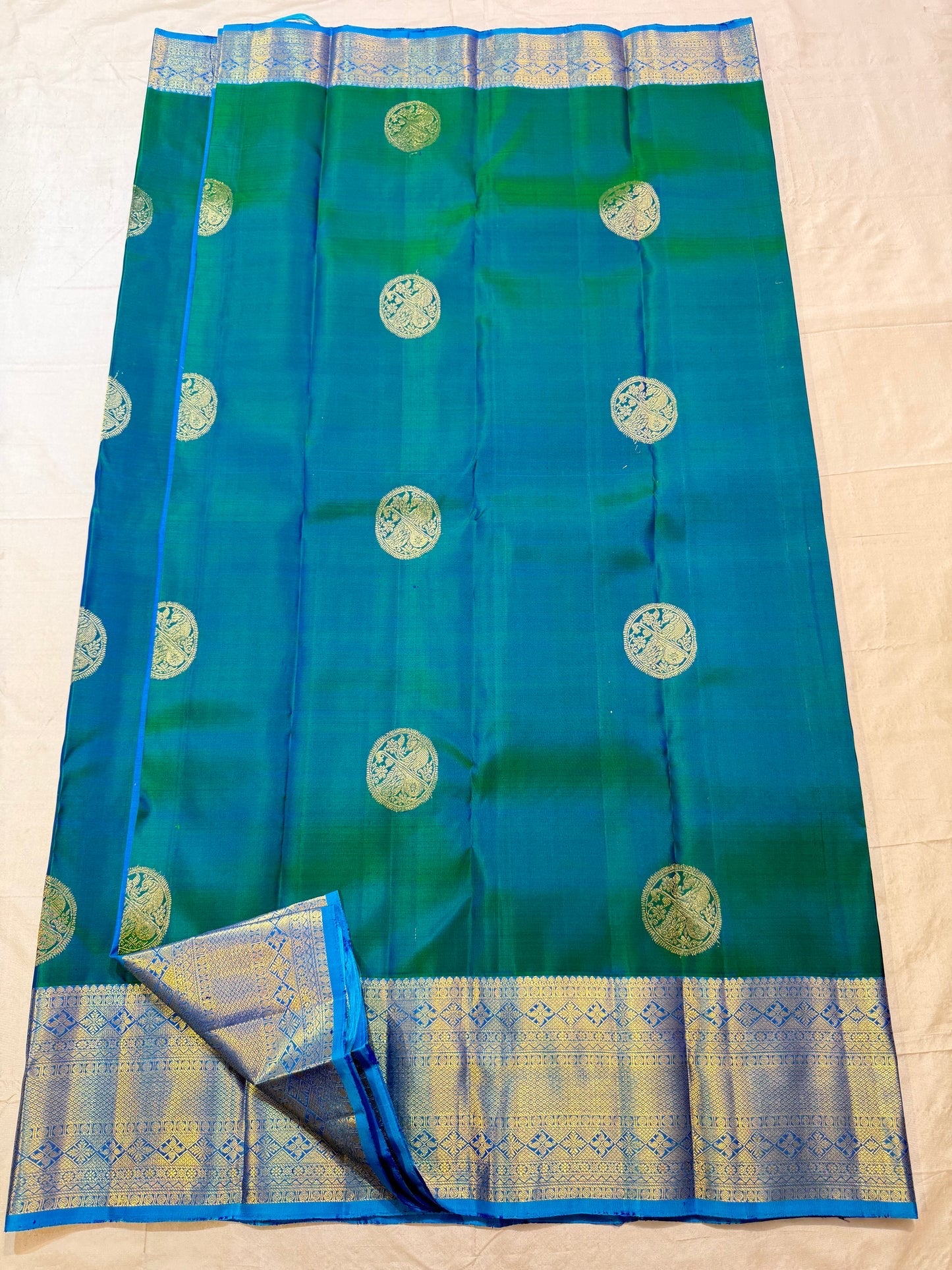 Peacock Blue and Green double-shade Kanchipuram silk showing large Veena-Peacock zari medallions and broad Sky Blue gold border.