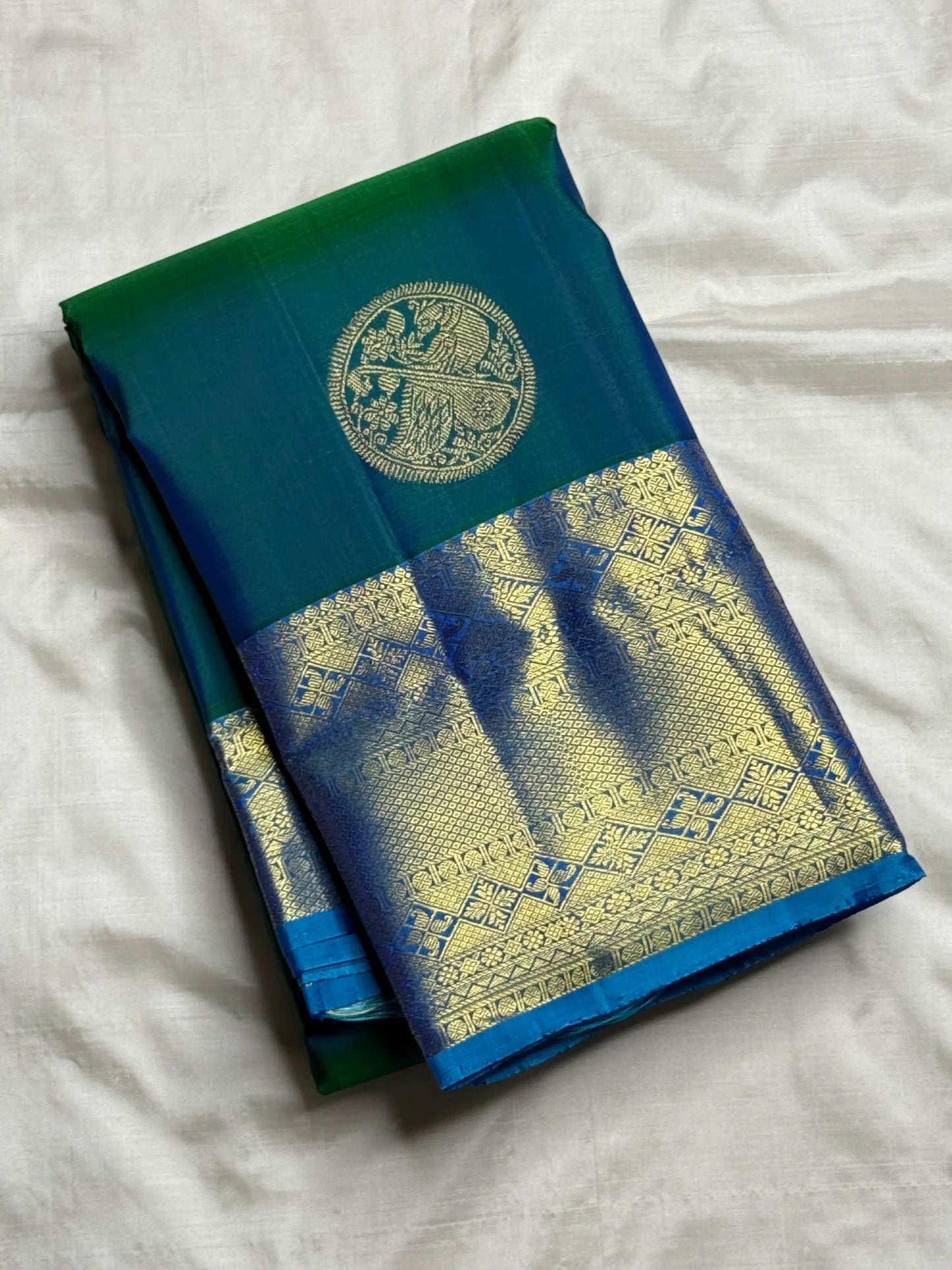 Peacock Blue-Green double-shade Kanchipuram saree showing gold Veena-Peacock medallion buttas and ornate Sky Blue zari border.