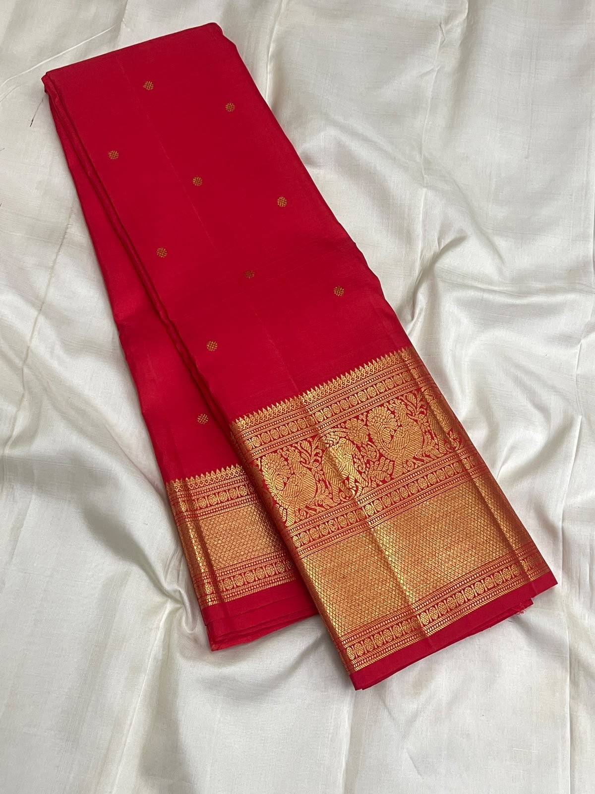 Vermilion Red Kanchipuram Butta saree with broad antique-gold geometric zari border.