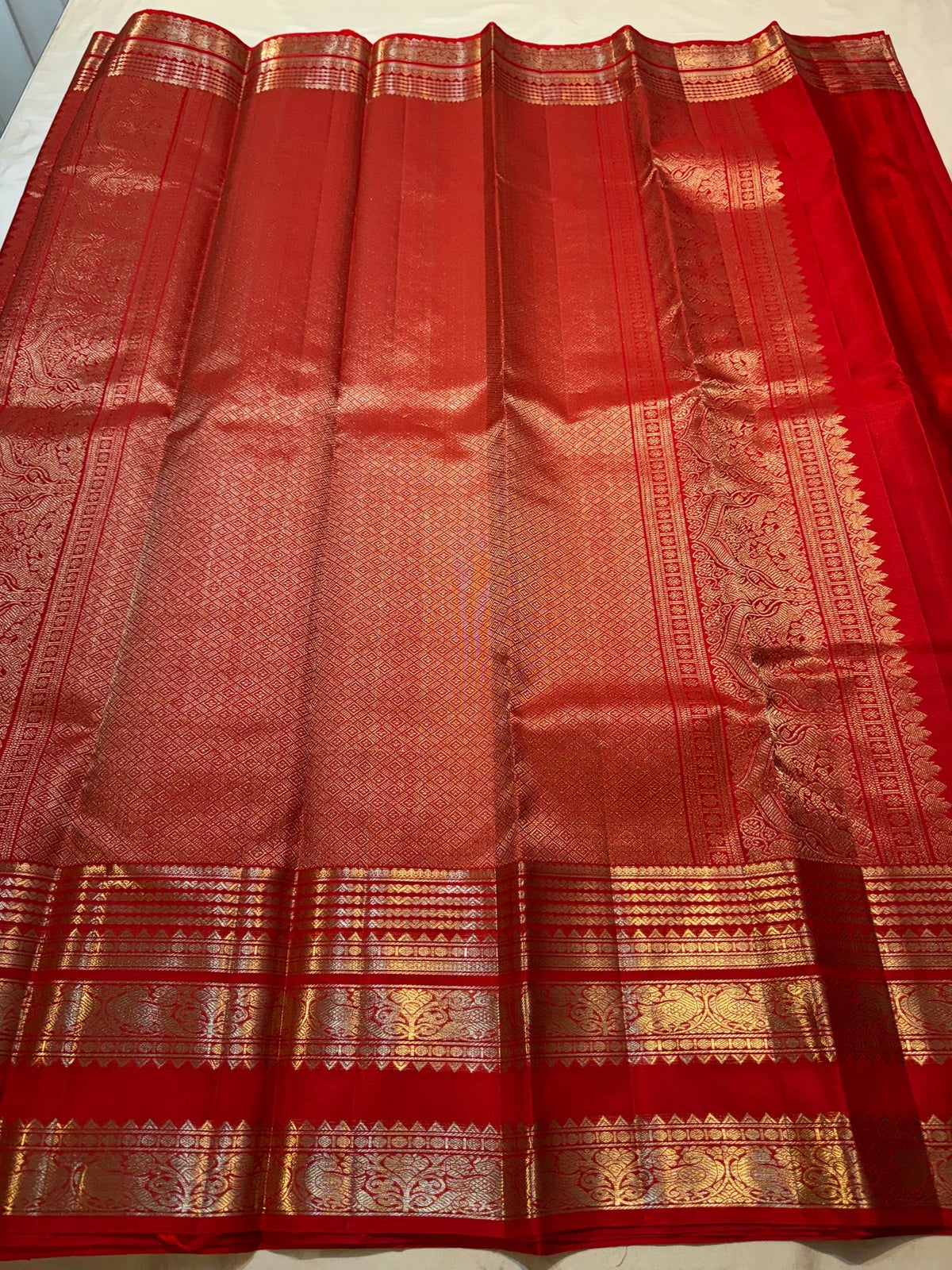 Red Kanchipuram saree border with repeated mayil motifs and layered geometric zari bands.