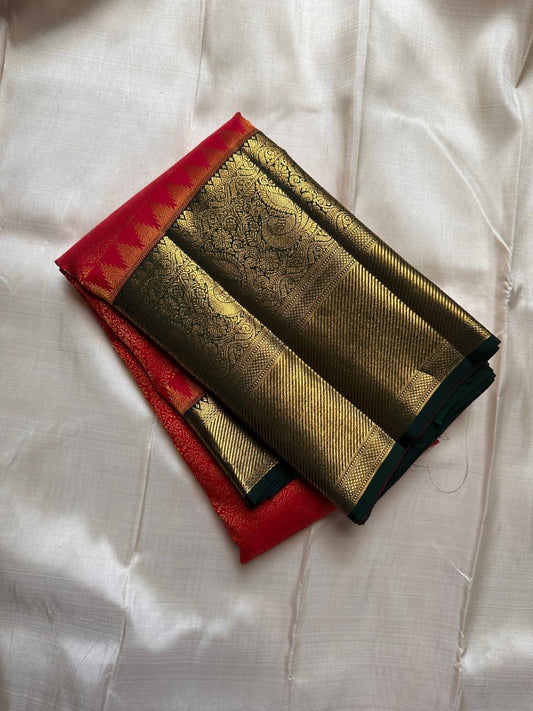 Folded Pure Kanchipuram silk saree showing a red body with a wide gold zari woven border and deep green edging.