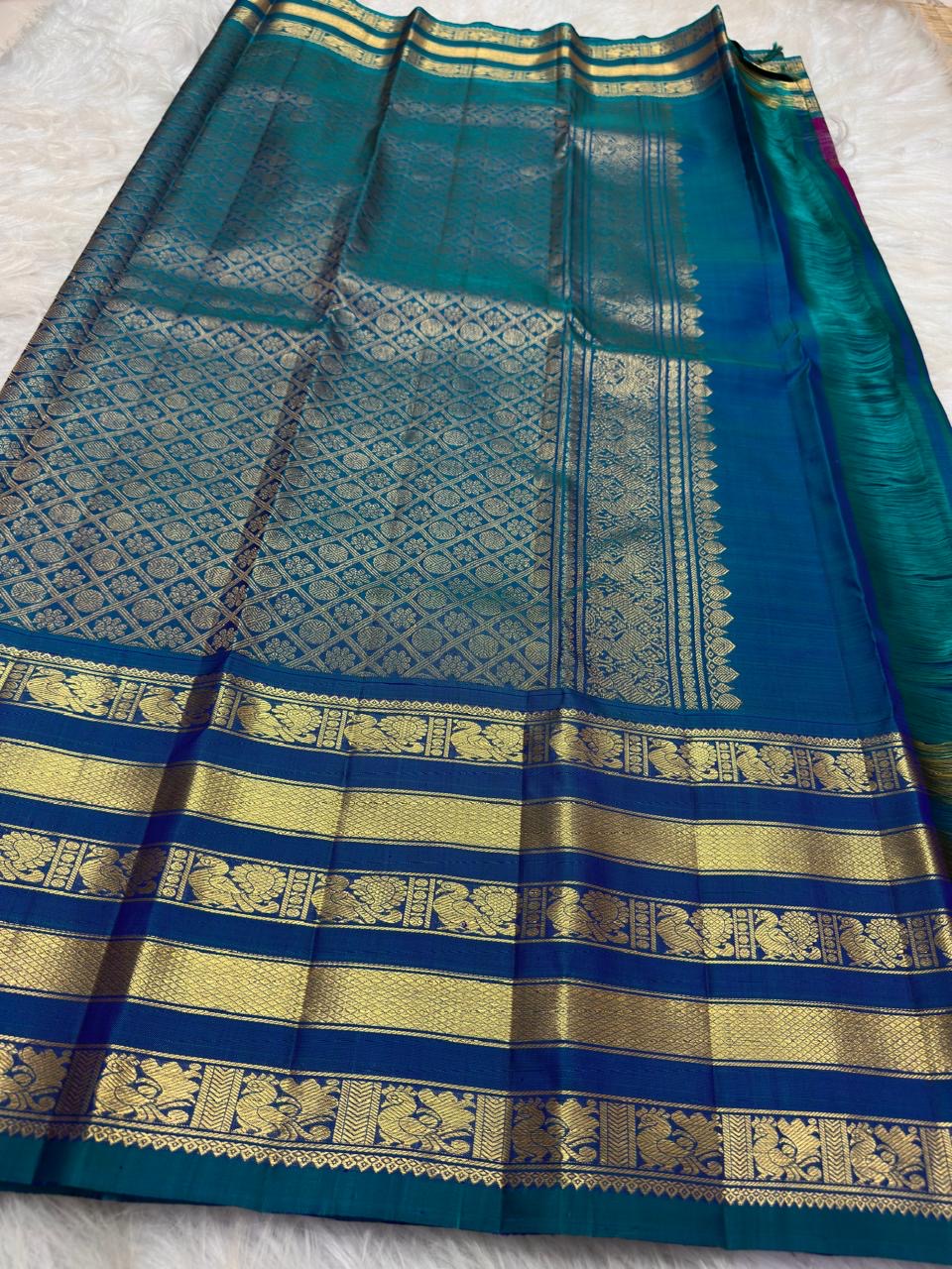 Neelam royal blue Varisaipet border with wide gold zari bands and peacock imagery on a magenta Kancheepuram saree