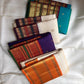 Folded Warm Ivory Varisaipet silk showing petite zari buttas and richly layered purple green gold border.