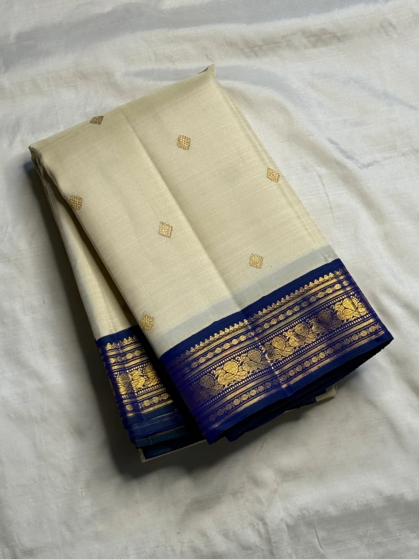 Warm Ivory Kanchipuram silk body with spaced gold zari buttas and peacock-neck colour Korvai border.