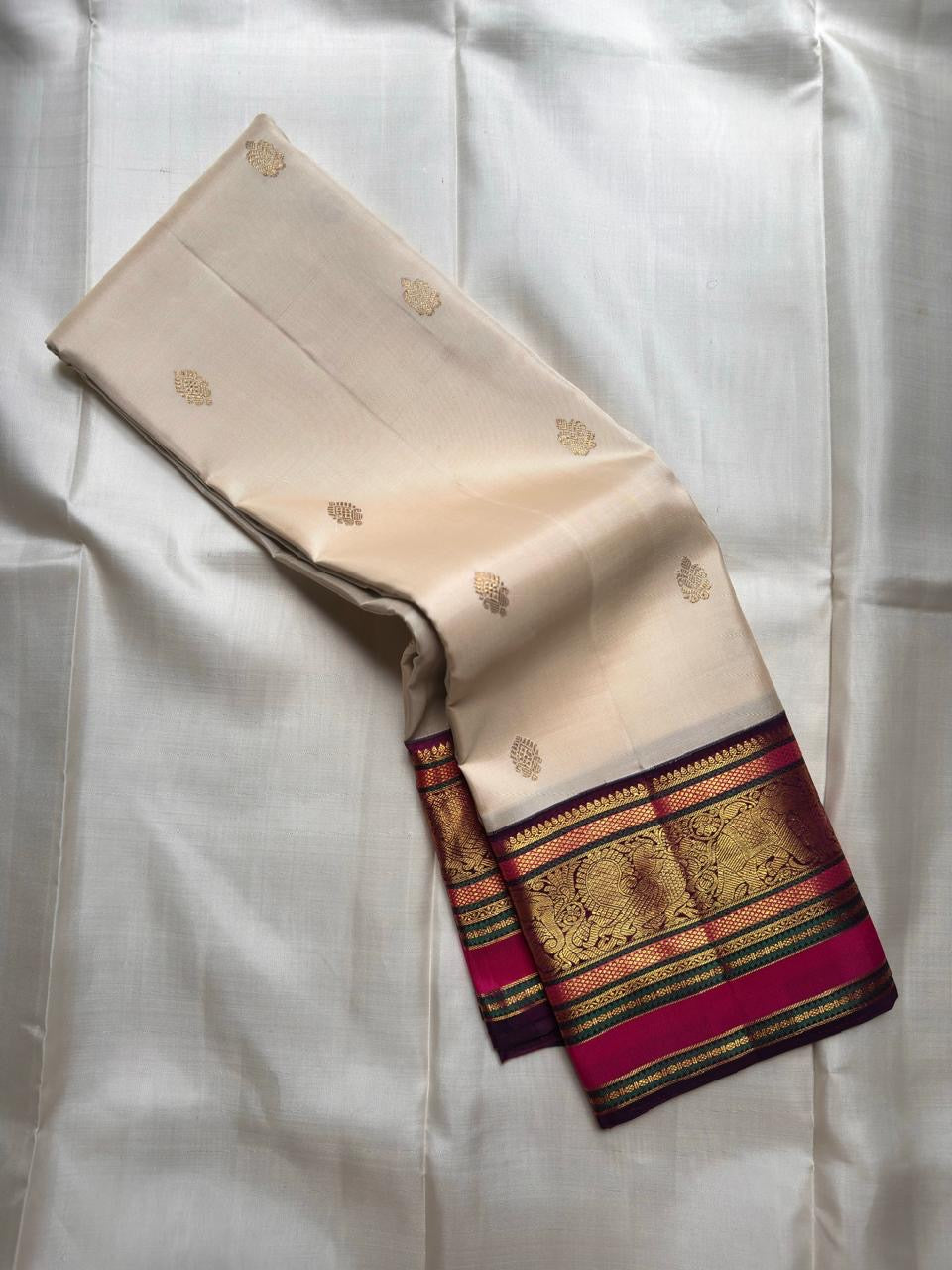 Warm Ivory pure silk KanchiPattu Butta saree with Vadamalli Magenta and gold zari border, shown folded.