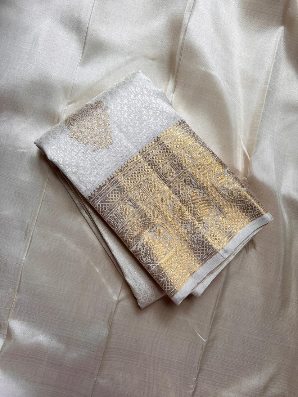 Folded ivory Pure Kanchipuram Silk Saree showing wide gold zari border on champagne silk background.