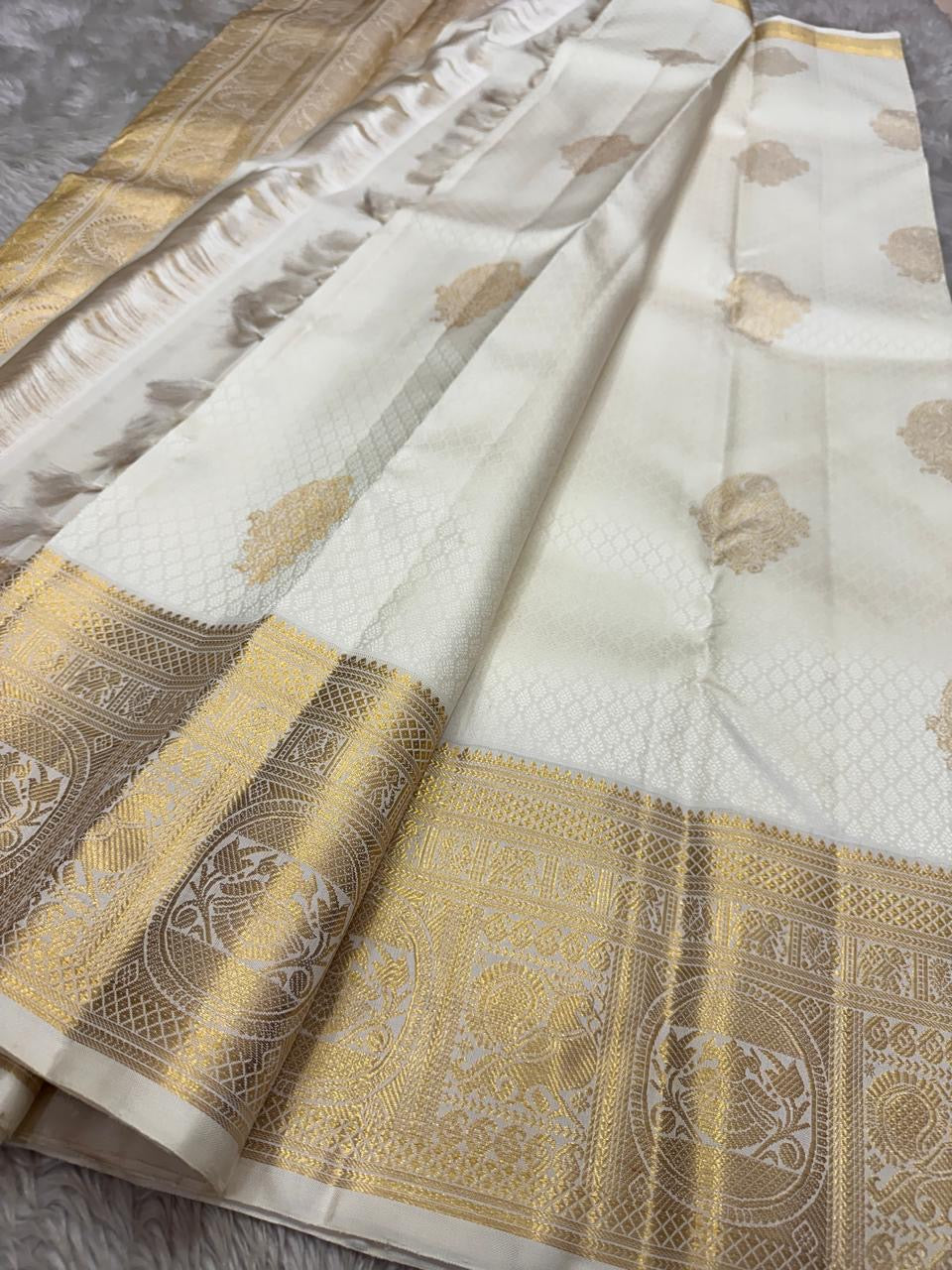 Flat lay of ivory Pure Kanchipuram Silk Saree with gold zari border and scattered gold motifs.
