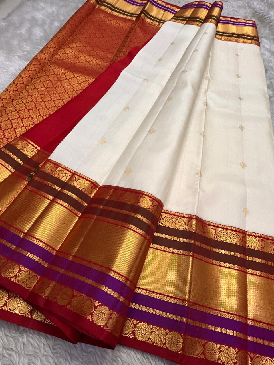 Full view of ivory Pure Kanchipuram silk saree with gold buttas, wide zari border, and a red pallu section with gold zari patterning.