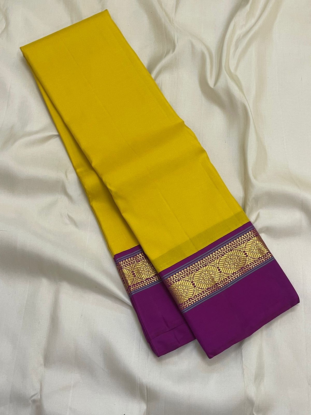 Pure Kanchipuram silk saree folded lengthwise showing yellow body and purple border with gold zari woven band