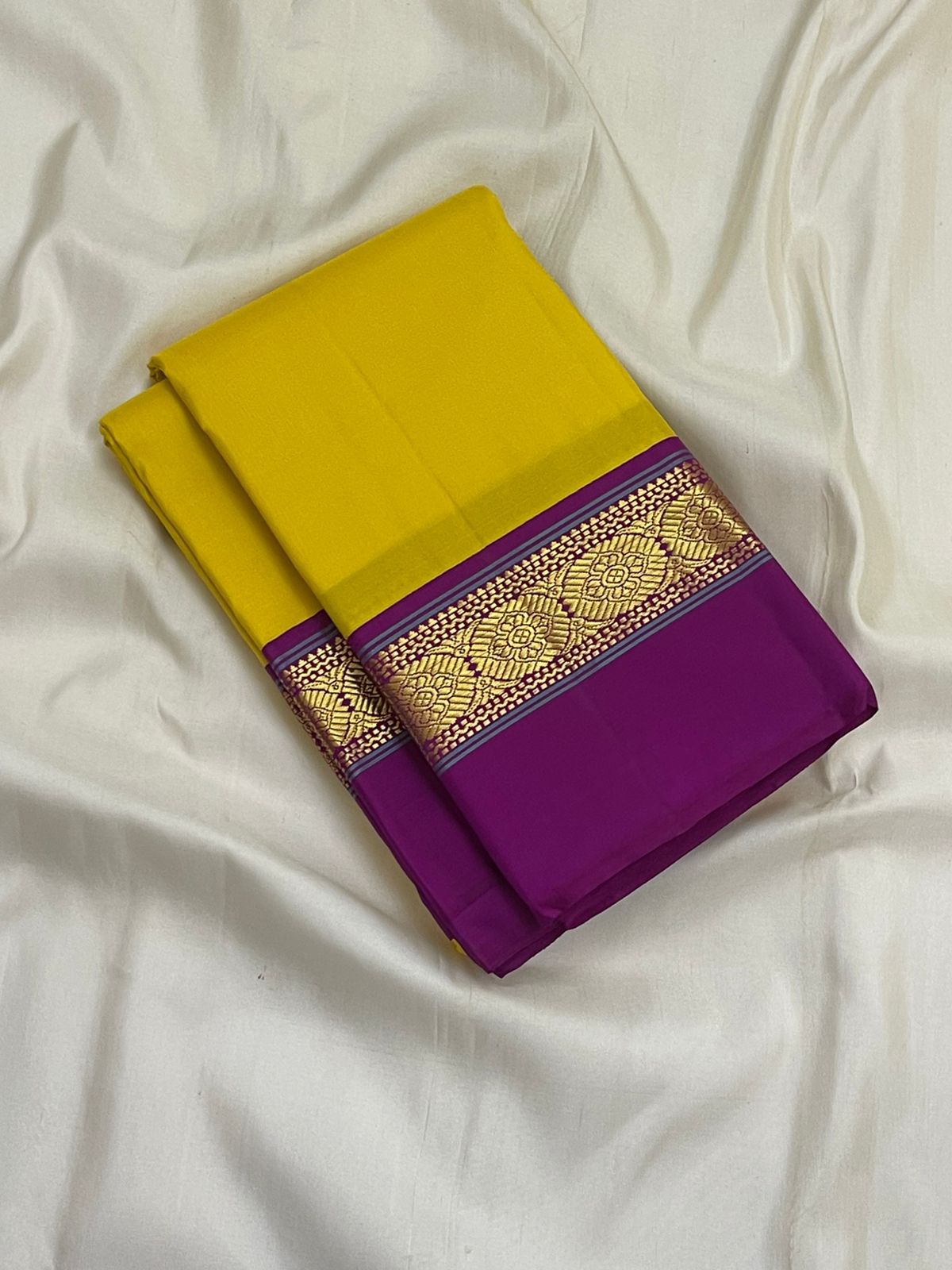 Folded pure Kanchipuram silk saree in bright yellow with wide purple border and gold zari woven motifs