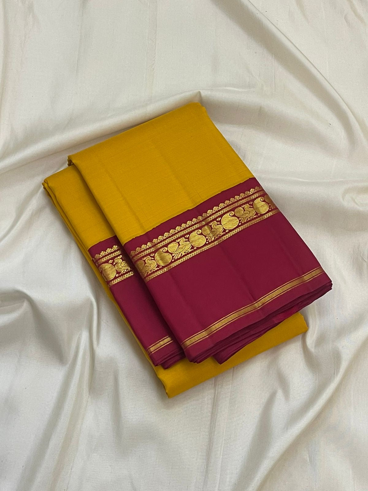 Canary yellow and arakku red Kanjeevaram silk saree folded showing plain body and contrast arakku red Korvai Kaal Irangiya border