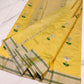 Folded Turmeric Yellow Pattu Silk Chanderi saree showing silver floral motif with green woven leaves and metallic striped border