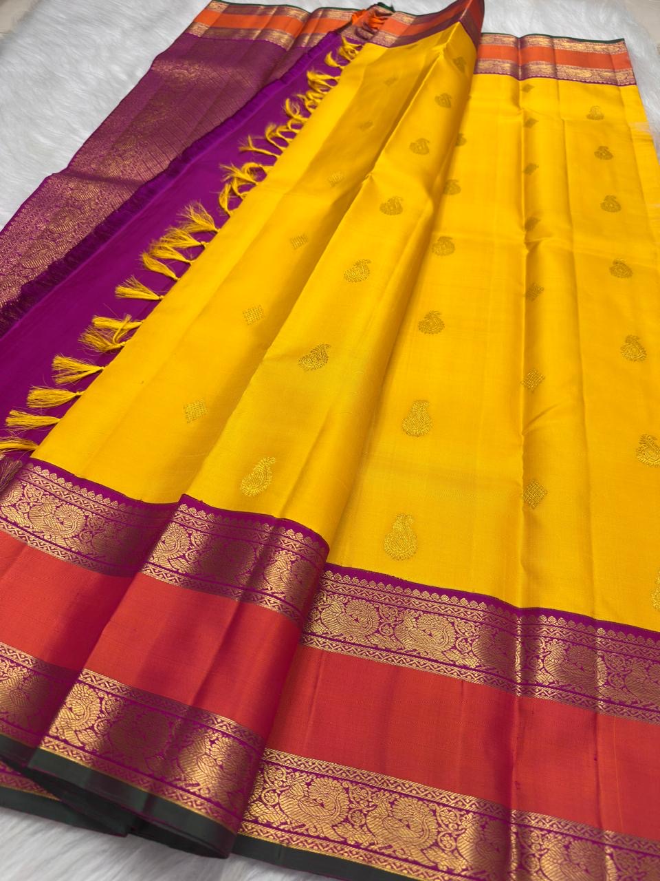 Yellow Korvai saree showing jewel-purple, coral-orange and antique-gold layered border details.